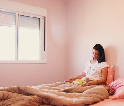 A woman relaxes with breakfast in bed in a cozy pink room, enjoying a peaceful morning.