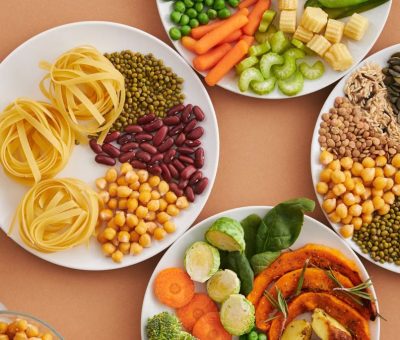 A vibrant mix of legumes, vegetables, nuts, and pasta arranged on white plates showcasing a balanced, healthy diet.