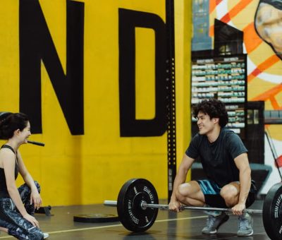 Two young adults in a gym participating in a weightlifting session, sharing a positive moment.